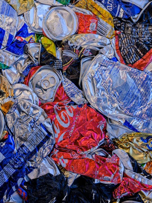 A sanitation worker, dressed in a bright orange reflective vest and dark trousers, is seen emptying the contents of a black plastic bag into a large red rubbish collection truck parked on the side of 